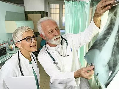 A male and female doctor, wearing lab coats, examine a set of chest x-rays.
