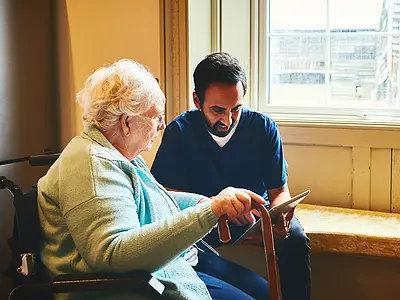 A senior woman and a male caregiver look at photos on a tablet.