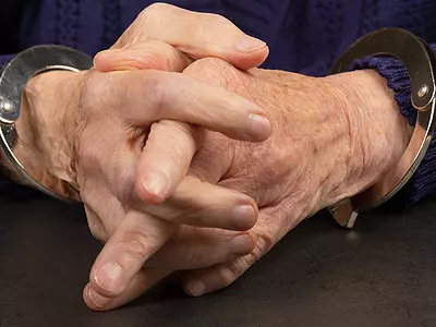 A closeup photo of a senior man's hands in handcuffs.