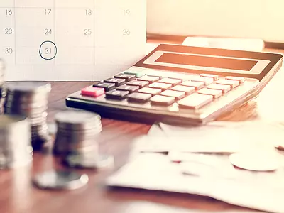 Photo illustration of a calendar, calculator, and money on a desk.
