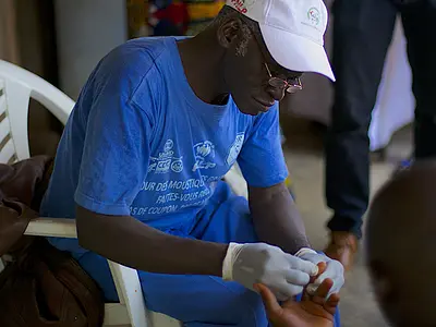 A worker takes a man's blood sample to test it for malaria as part of the Stop Palu program in Guinea.