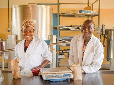 An African woman and man in white coats smiling in front of equipment