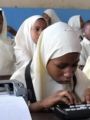 Girls with visual impairments practice reading in a classroom in Zanzibar.