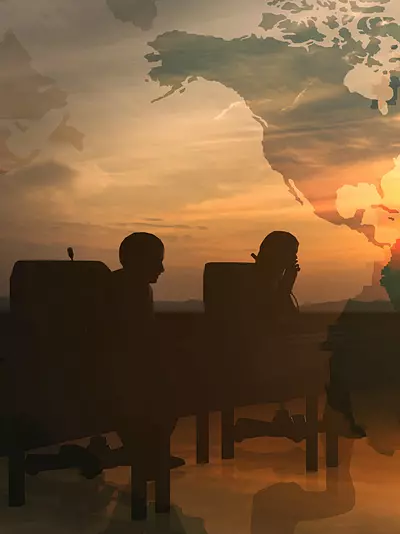 A group of professionals talk while silhouetted in front of a large world map.