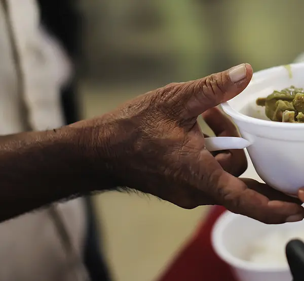 Closeup of hands passing a bowl of vegetables to a man standing at a counter.