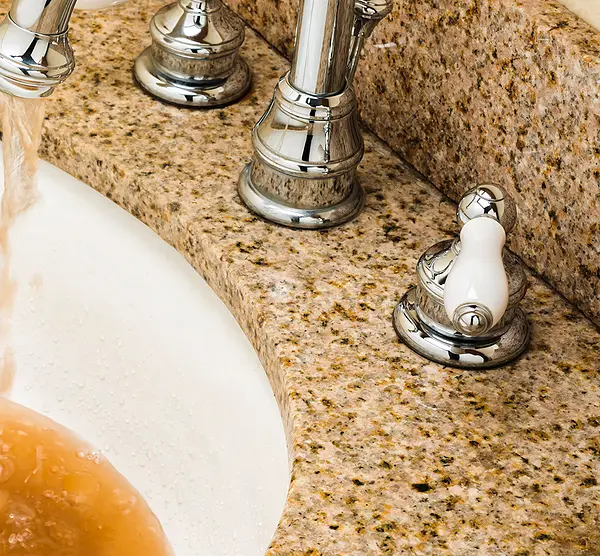 Discolored, polluted water pours from a faucet into a bathroom sink.