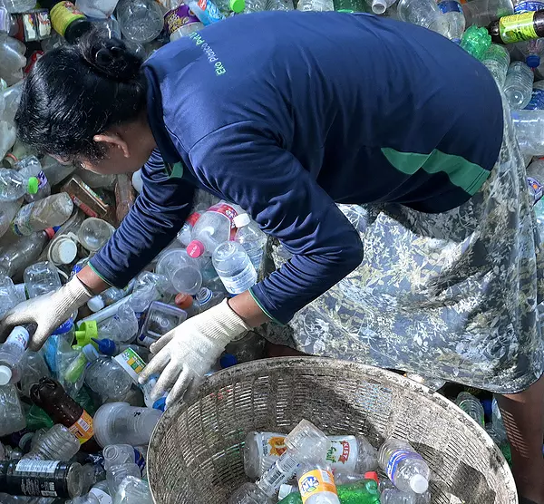 A woman collects bottles from a heap of plastic waste.