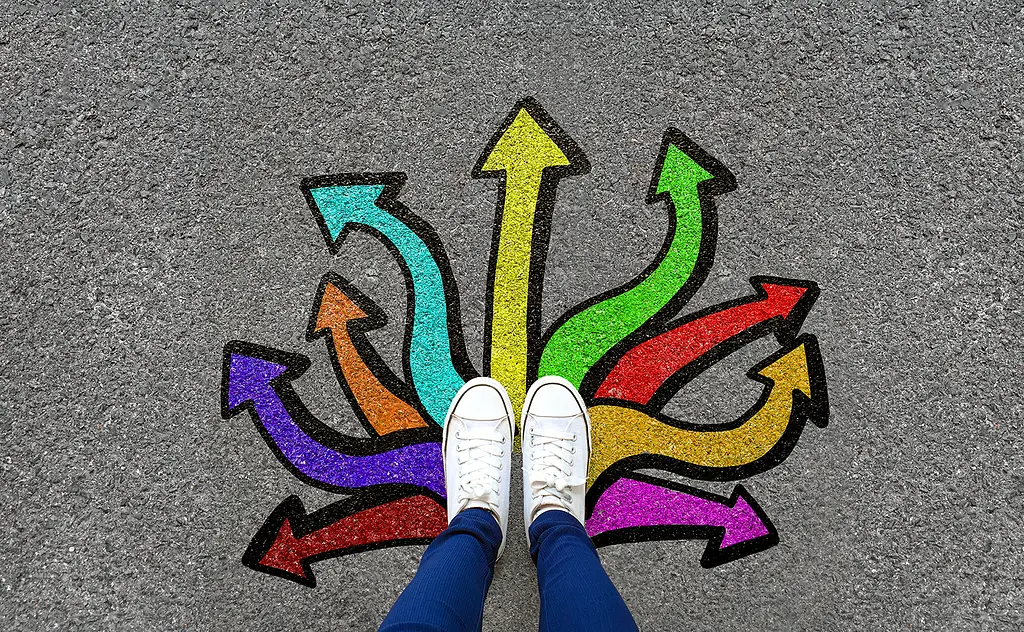 A pair of feet, wearing sneakers and jeans, on pavement painted with colorful arrows.