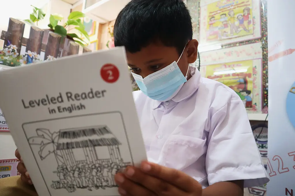 Child with a mask reads a book in English in a classroom