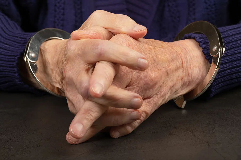 A closeup photo of a senior man's hands in handcuffs.