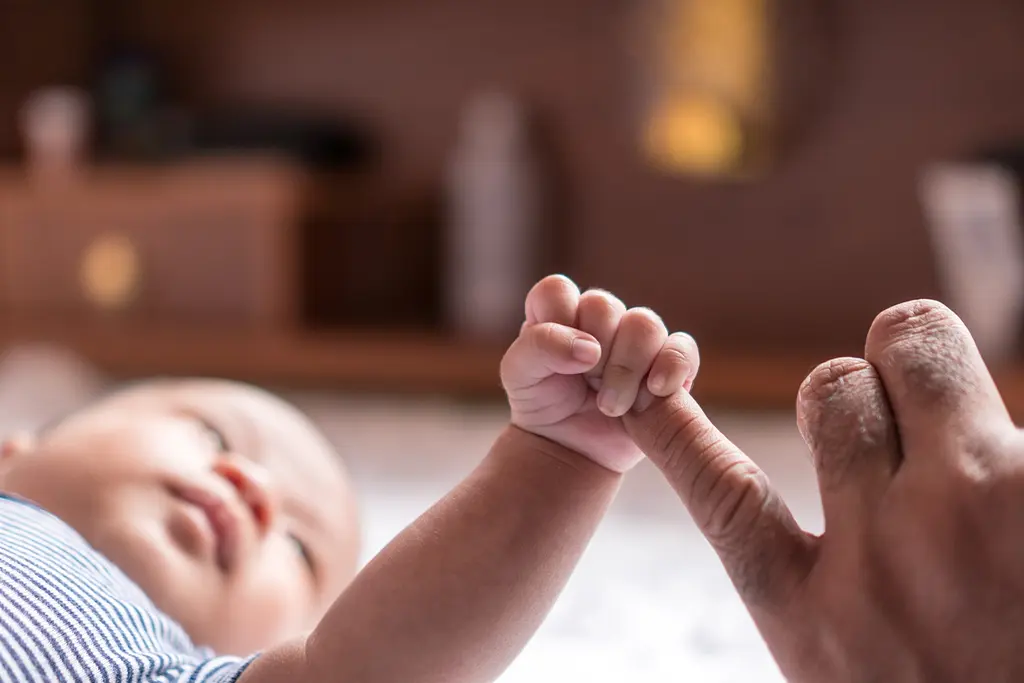 A closeup photo of a baby holding an adult's pinky