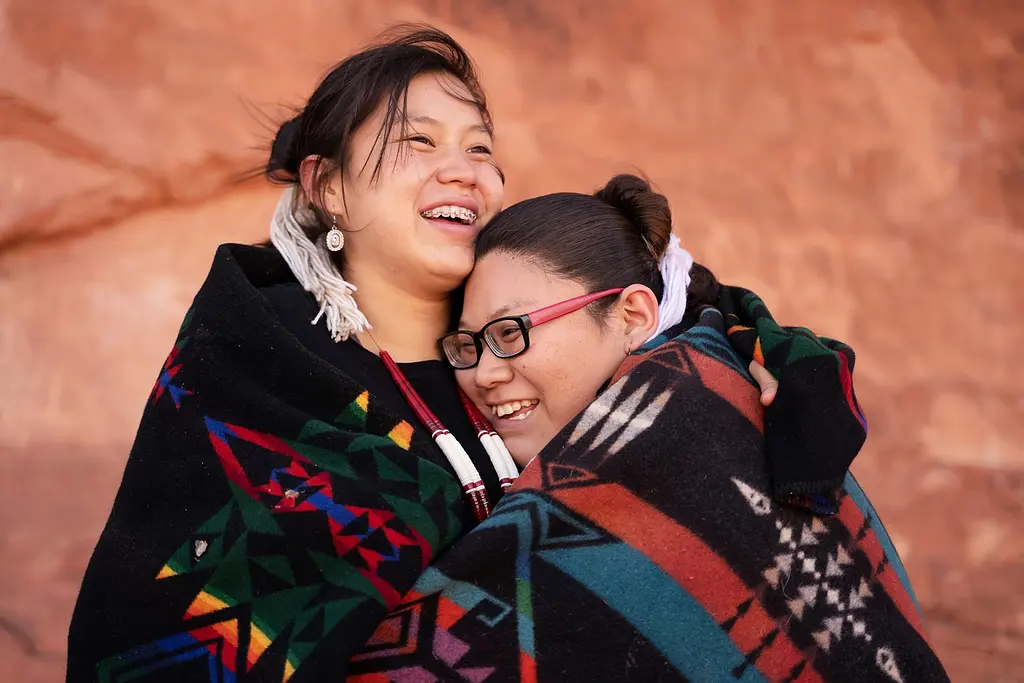 Photo of two Navajo sisters outdoors hugging and smiling