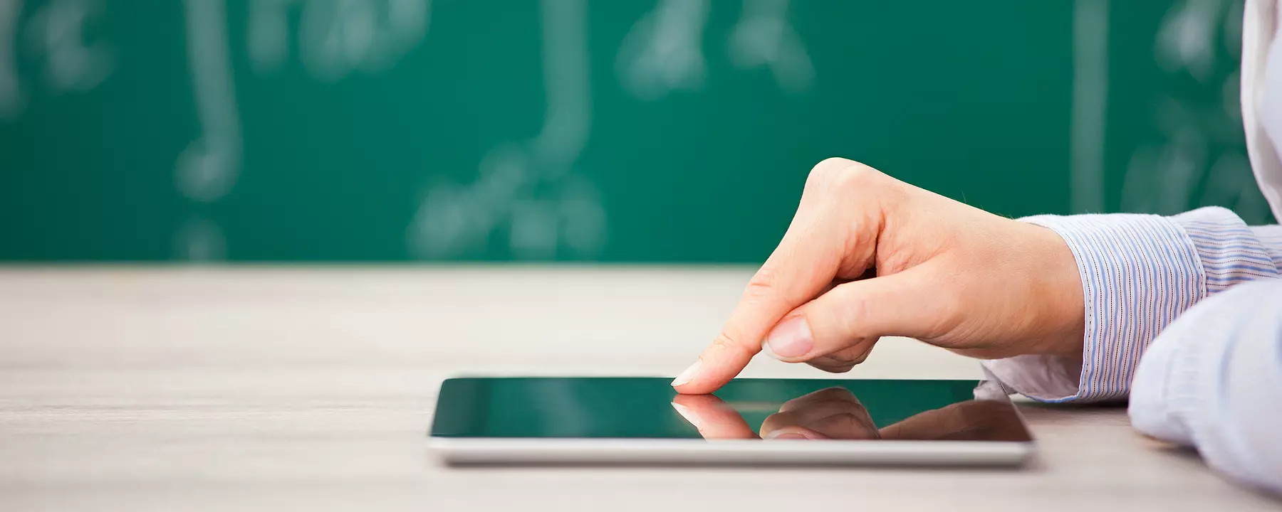 A person uses a tablet in front of a chalkboard in a classroom