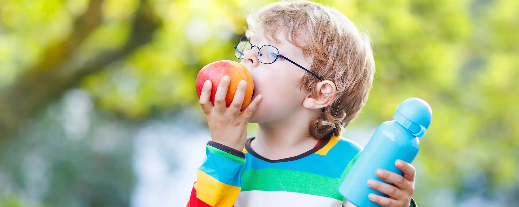 A boy eating an apple and holding a water bottle