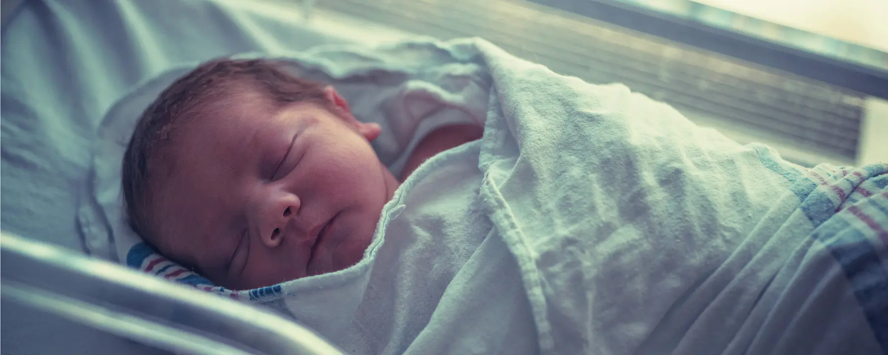 A newborn baby sleeps in a hospital crib