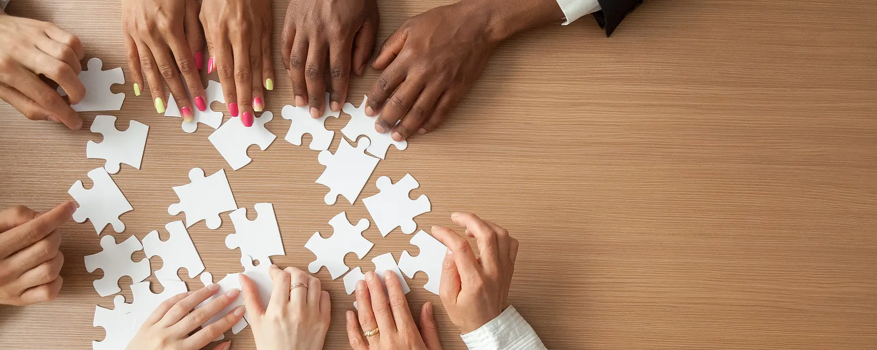 A closeup of people's hands as they work together to assemble a puzzle.