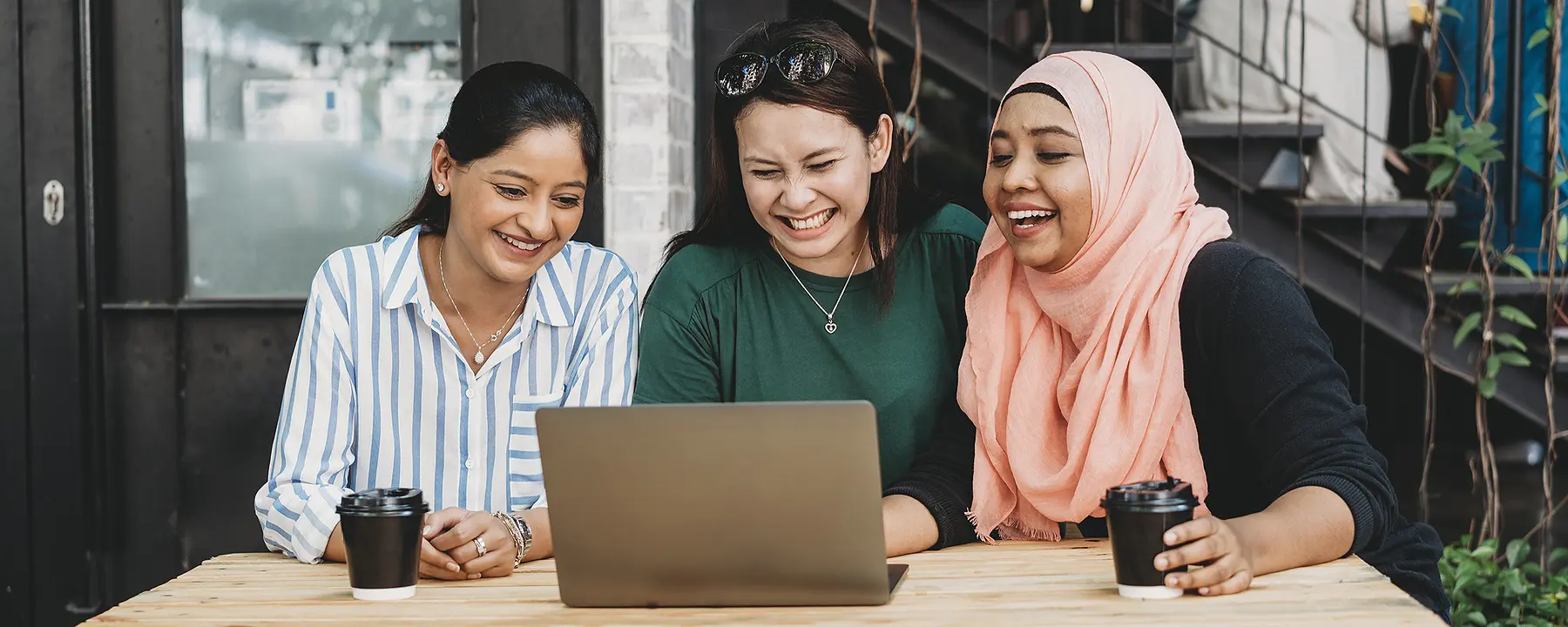 Three women using the internet at an outdoor cafe in Malaysia