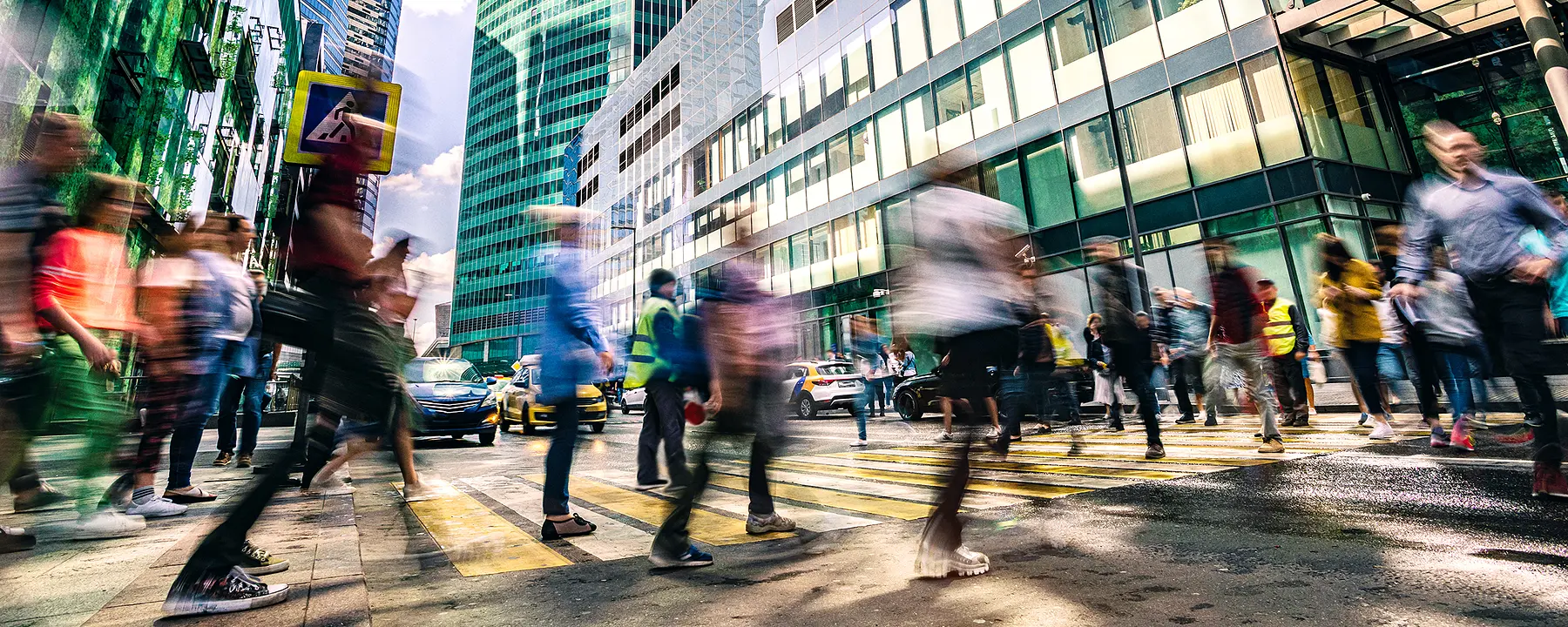 An evening city scene with pedestrians crossing a busy intersection.