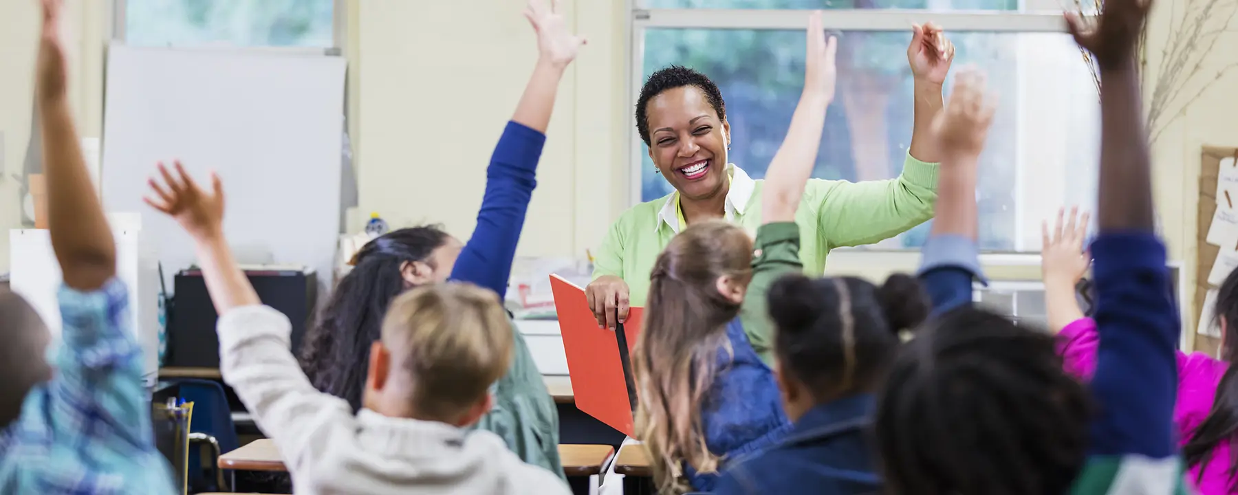 Teacher in a classroom with kids raising their hands