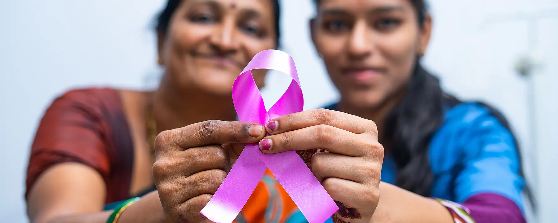 Two Indian women hold a ribbon symbolizing cancer awareness.