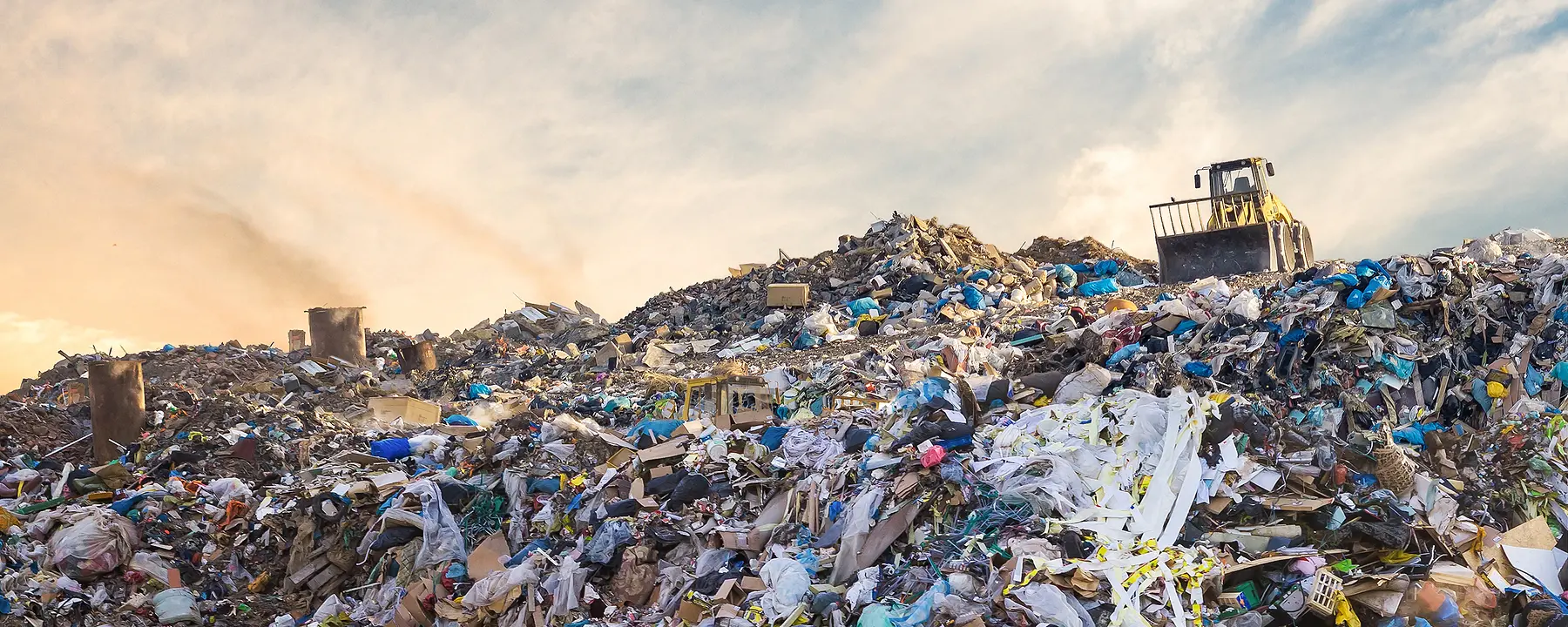 A bulldozer sits atop a heap of garbage in a large landfill.