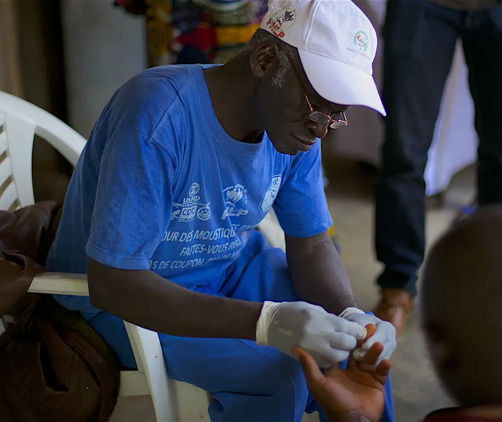 A worker takes a man's blood sample to test it for malaria as part of the Stop Palu program in Guinea.