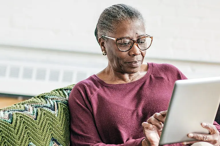 A senior Black woman wearing glasses checks out a website on a tablet.