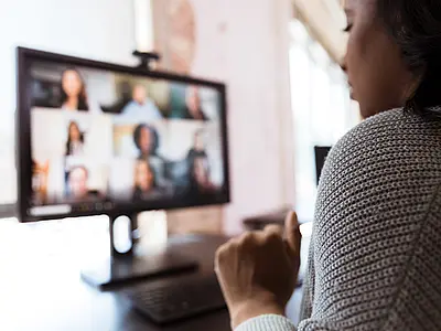 A woman watches her colleagues on a video call.