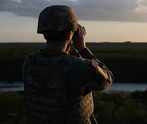Military personnel looks through binoculars
