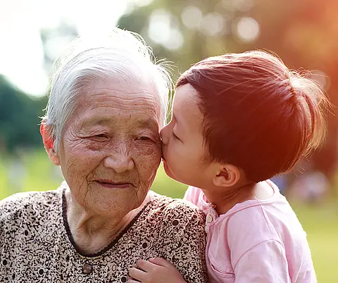 An older Asian woman gets a kiss from her grandchild.