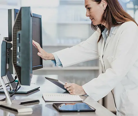 A female scientist in a white lab coat works with a touchscreen computer.